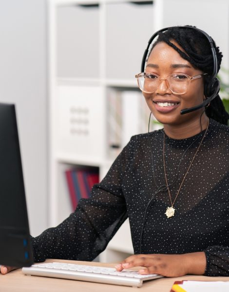 Customer service agent, financial advisor call center employee sits at desk in company in front of computer screen, headphones with microphone on ears, connecting with caller, solving problem.